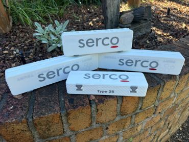 Four Serco branded white boxes on a brick surface.