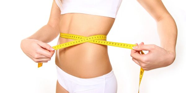 Woman measuring her slim waist with a yellow tape measure.