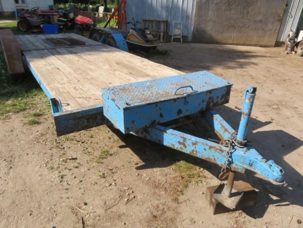 Rusty blue flatbed trailer with wooden deck parked on dirt ground.