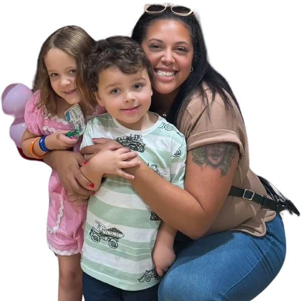 A smiling woman crouches with two young children, hugging them closely.