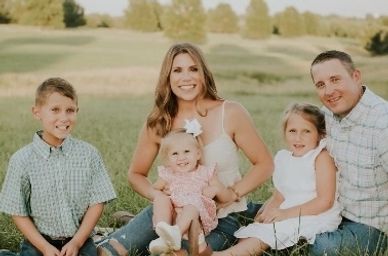 A happy family of five posing outdoors in a sunny field.