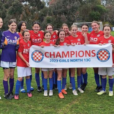Group of girls from Under 13s soccer team holding a banner saying 'Champions'