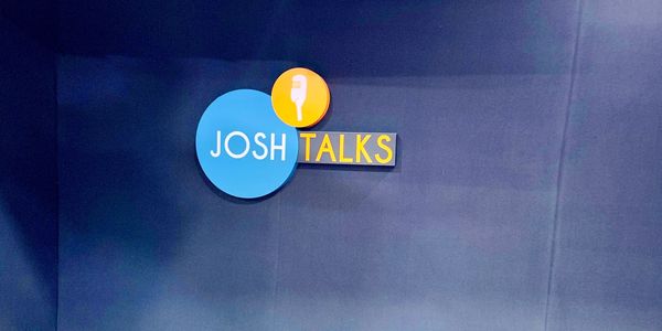 Logo of Josh Talks on a dark blue wall.