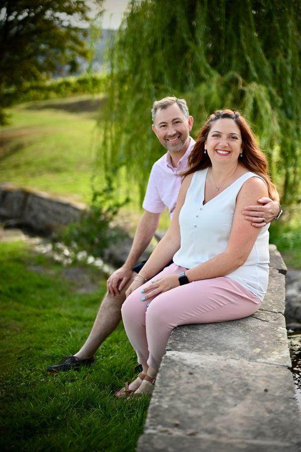 Smiling couple sitting on a stone ledge in a lush green park.