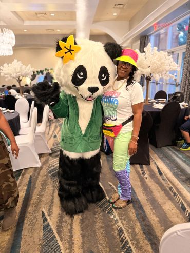 Person posing with someone in a panda costume indoors.