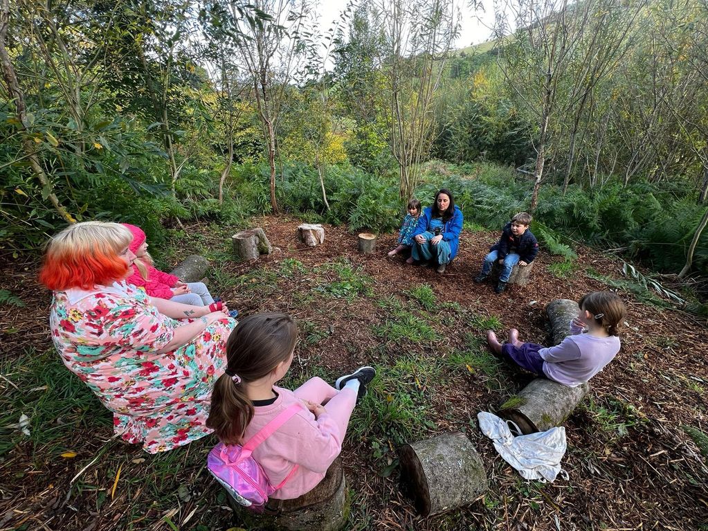 Forest school speech therapy session children, parents and therapist sitting around log circle
