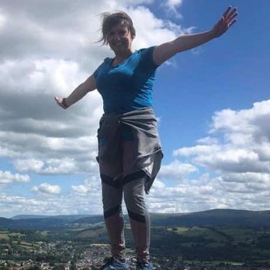 Woman balancing on a trig point in Wales 