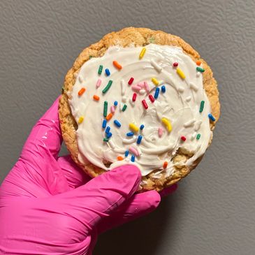 Hand in pink glove holding a frosted cookie with sprinkles.