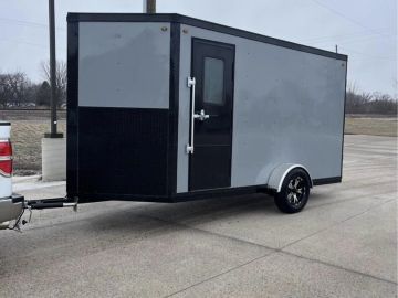 A gray cargo trailer attached to a vehicle on a concrete surface.
