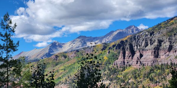 Mountain landscape with rocky cliffs and trees under a blue sky.