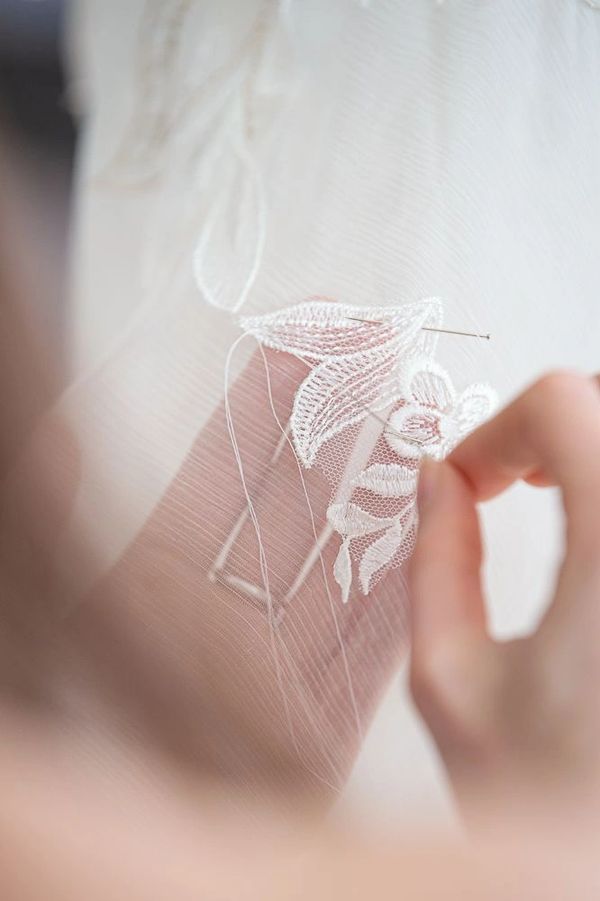 Hand sewing delicate white lace onto sheer fabric with a needle.