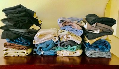 Three stacks of folded clothes on a wooden surface.