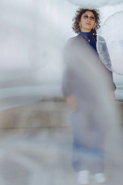 Woman with curly hair and glasses standing behind a translucent surface.