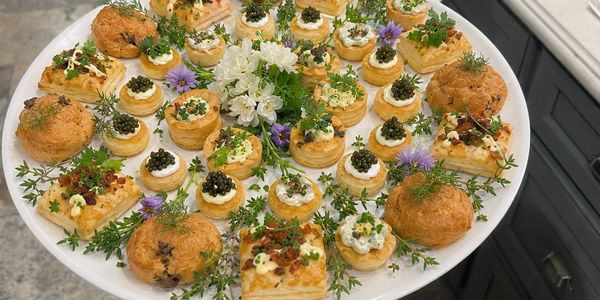 Elegant platter of assorted gourmet appetizers with herbs and flowers.