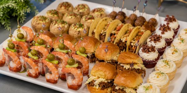 Assorted appetizers including shrimp, sliders, tacos, cupcakes, and stuffed mushrooms.