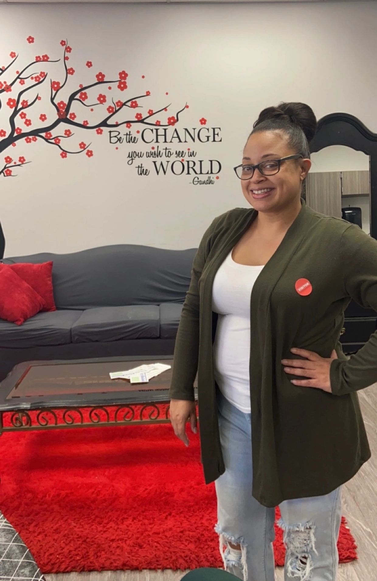 Smiling woman standing in a cozy room with inspirational wall art and vibrant red accents.