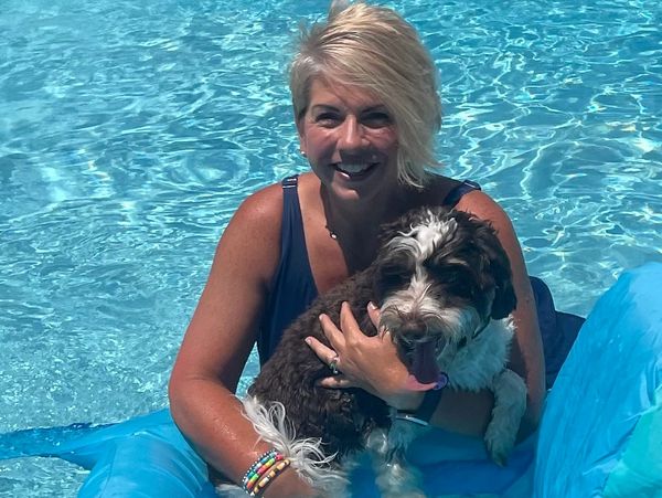 Woman smiling and holding dog in a pool.