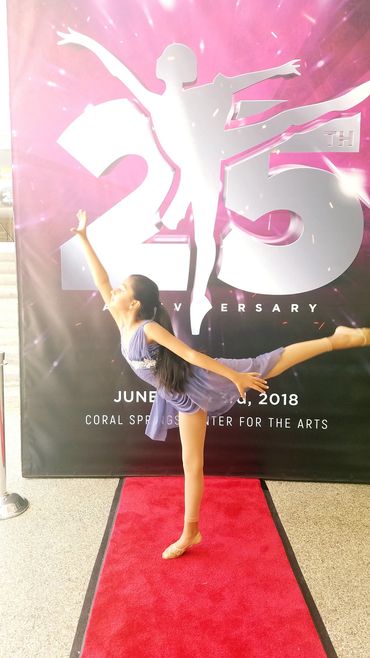 Young ballerina posing on red carpet at anniversary event.