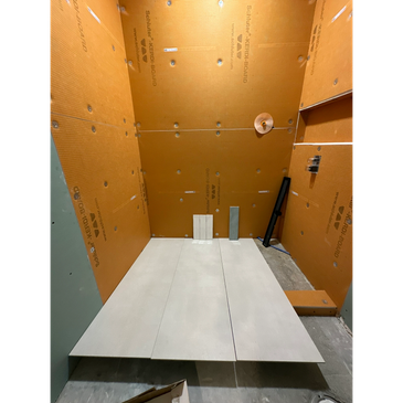 A shower under construction with orange waterproof backer boards and large floor tiles.