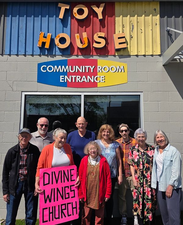 Group of seniors outside Toy House community room holding Divine Wings Church sign.