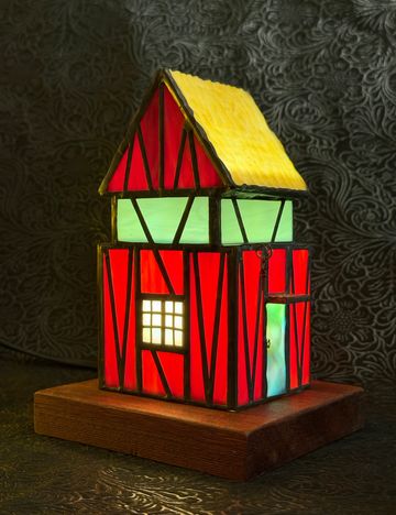 Illuminated stained glass house on wooden base.