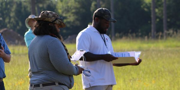 Two people outdoors reviewing documents and equipment.