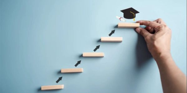 Hand placing wood block with graduation cap at the top of wooden steps.