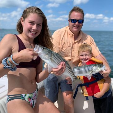 Family proudly shows off their striped bass catches on a sunny boat trip.