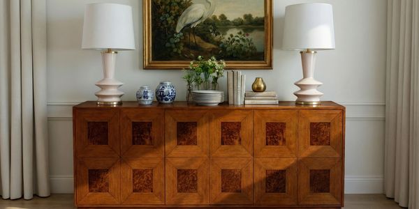 Elegant wooden sideboard with lamps and decorative items under a bird painting.