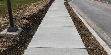 Newly paved concrete sidewalk alongside a road with fresh soil on both sides.