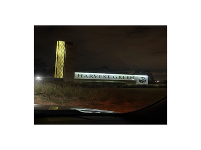 Illuminated Harvest Green entrance sign at night with decorative tower.