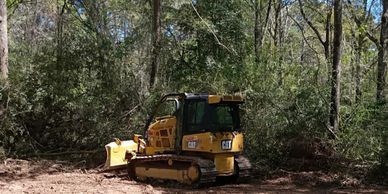 Yellow Caterpillar bulldozer clearing wooded area.