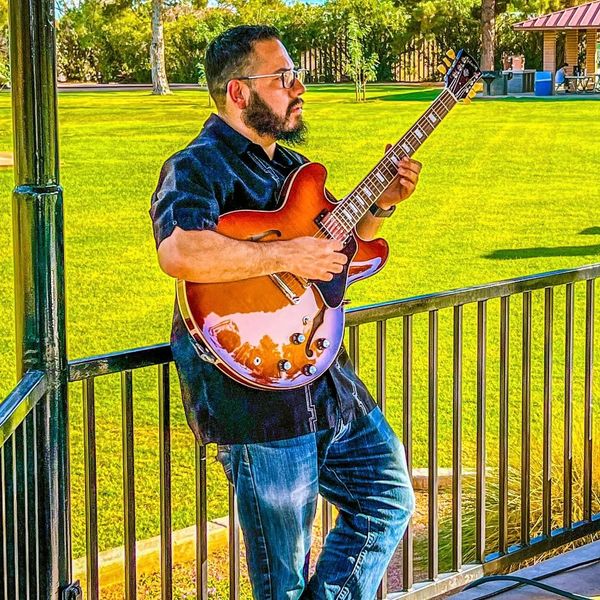 Man playing an electric guitar outdoors on a sunny day.