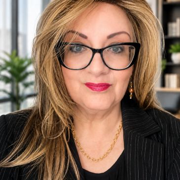 Professional woman with glasses and blonde hair in an office setting.