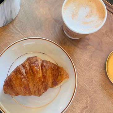 A croissant on a wooden table with a latte drink.