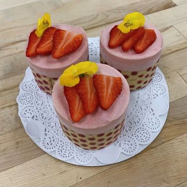 Three pastries topped with fresh strawberries and edible yellow flowers on a butcher block table.