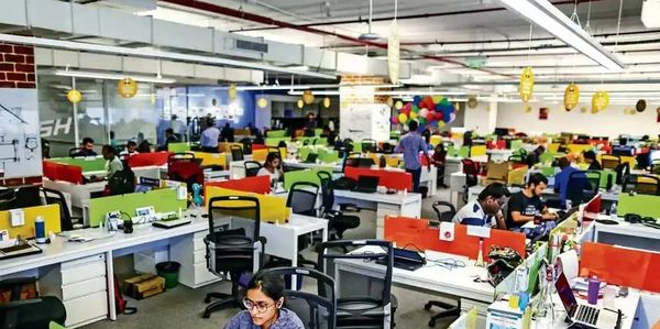 A busy modern office with employees working at colorful desks.