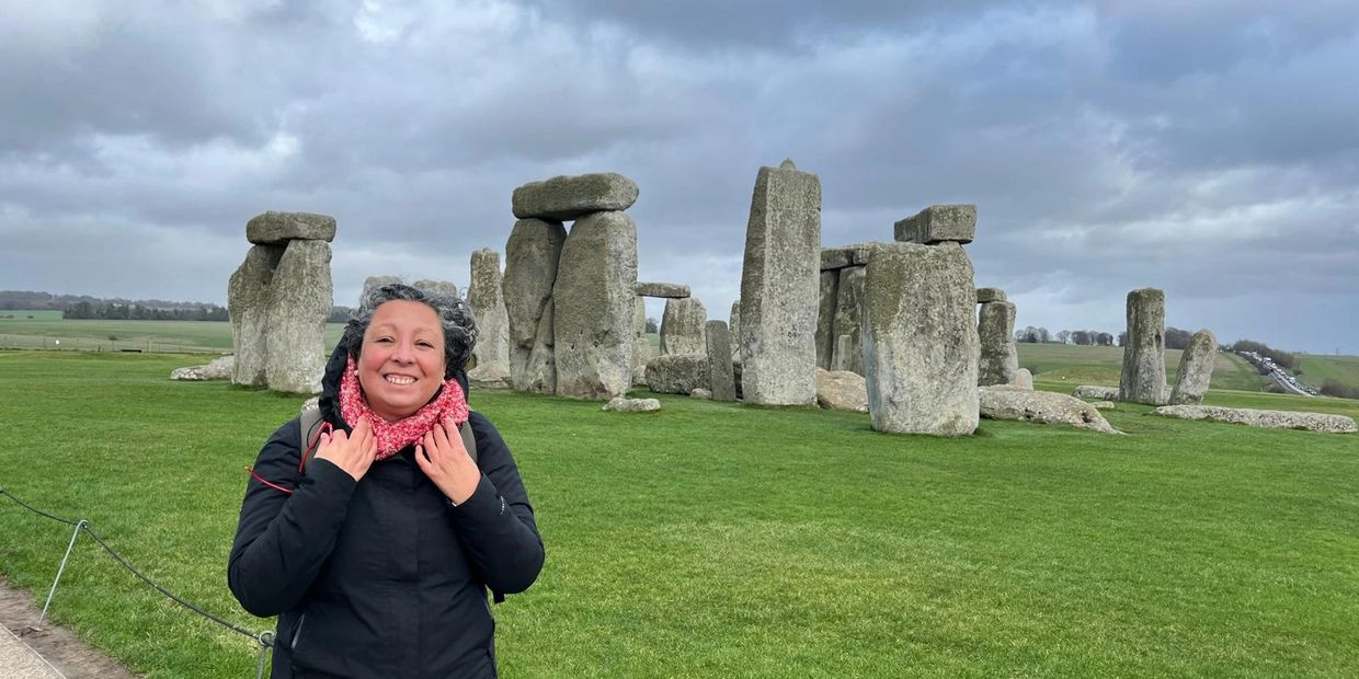 A smiling woman stands in front of Stonehenge on a cloudy day.