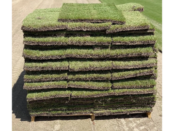 Stack of fresh sod rolls ready for installation on a lawn.