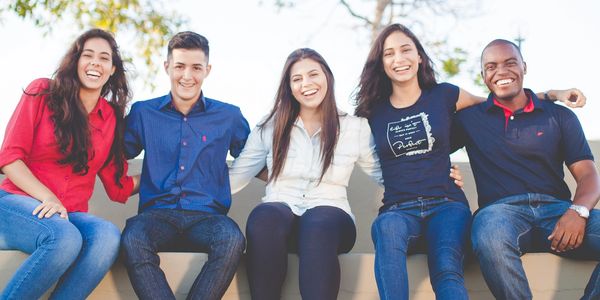 Happy English students from Brazil sitting on a bench outside having fun with arms around each other