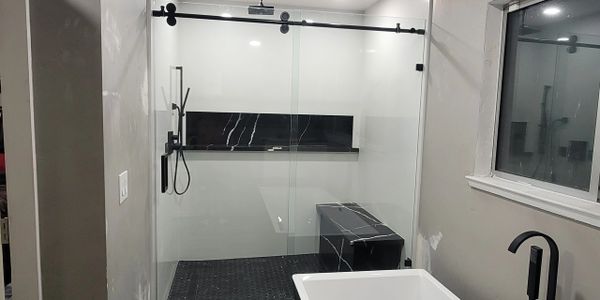 Modern bathroom with black and white design and glass shower enclosure.