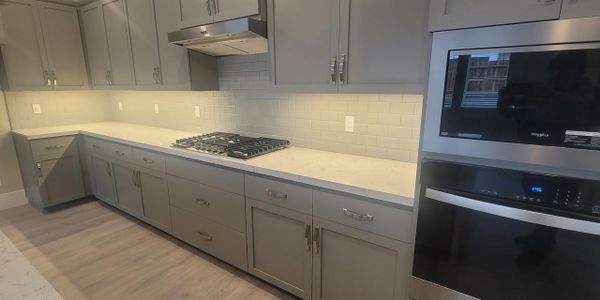 Modern kitchen with gray cabinets, white countertops, and built-in stainless steel appliances.
