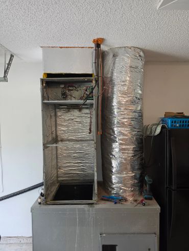 Exposed HVAC unit with ductwork and tools on top, in a garage setting.