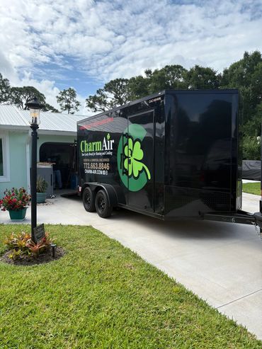 Black Charm Air trailer parked in a residential driveway beside a lamp post and green lawn.