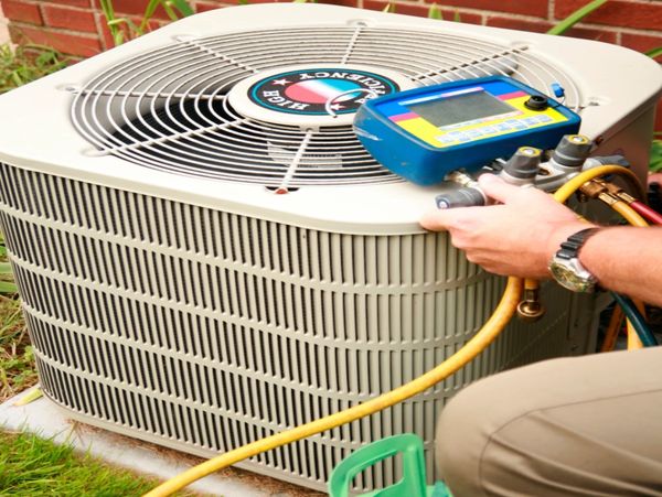 Technician servicing an outdoor air conditioning unit with diagnostic tools.