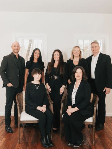 A group of seven professionally dressed people posing indoors against a white wall.