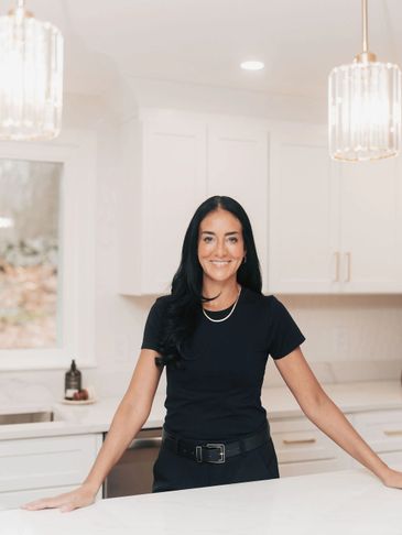 Smiling woman in black standing confidently in a bright modern kitchen.
