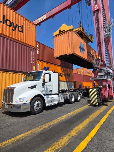 Truck loading a shipping container at a port crane.