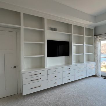 White built-in shelving and drawers under a mounted flat-screen TV in a bright room.