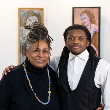 Two people posing in front of portrait paintings in an art gallery.